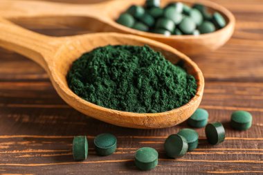 Bir kaşık spirulina tozu ve tahta arka planda haplar, yakın plan.