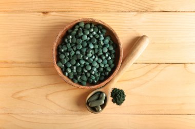 Tahta arka planda bir kase spirulina tozu, kaşık ve haplar.