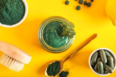 Bir kavanoz spirulina yüz maskesi, haplar ve sarı arka planda toz.