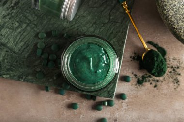 Bir kavanoz spirulina yüz maskesi ve grunge arkaplanda haplar olan tahta.