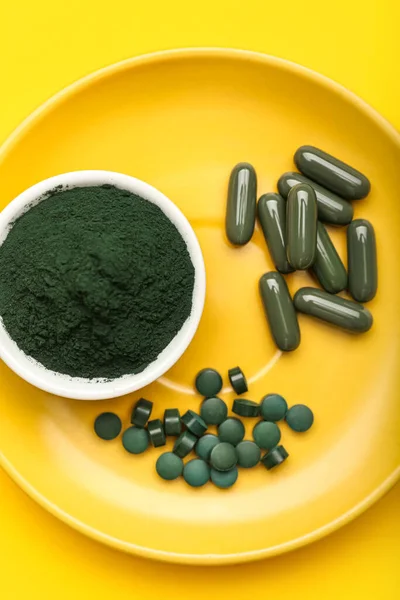 Bir kase spirulina tozu ve sarı arka planda haplar.