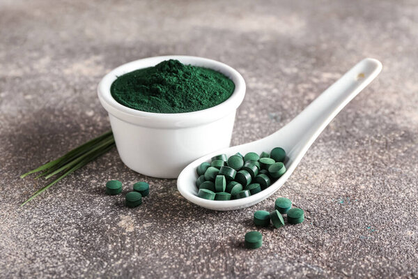 Миска спирулина порошок, ложка и таблетки на фоне гранж