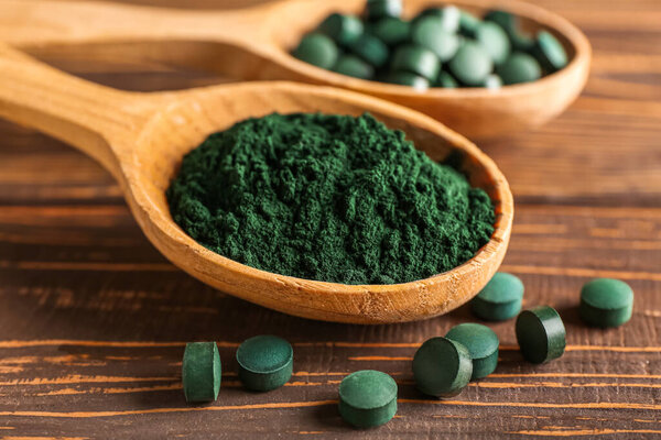 Spoon of spirulina powder and pills on wooden background, closeup