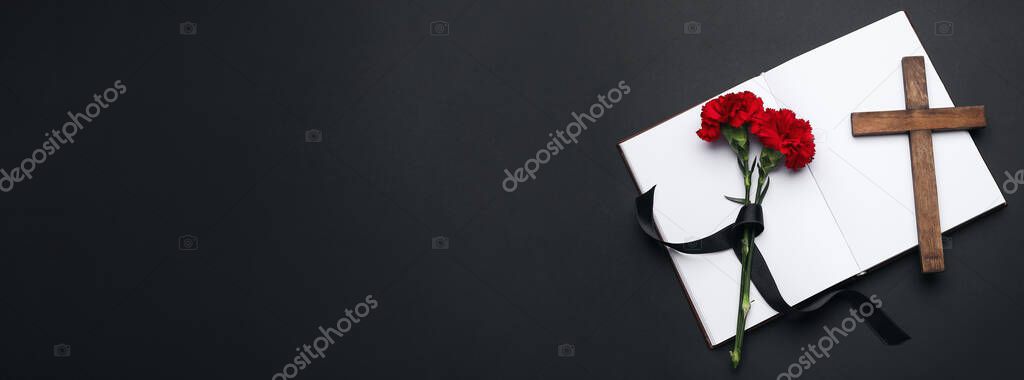 Book, carnation flowers, funeral ribbon and cross on black background with space for text