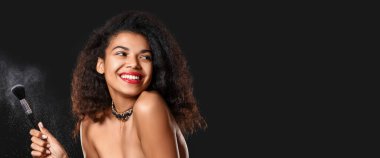 Siyah arka planda makyaj fırçası olan güzel bir Afro-Amerikalı kadın portresi.