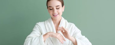 Bornozlu güzel bir kadın yeşil arka plana krem sürüyor.