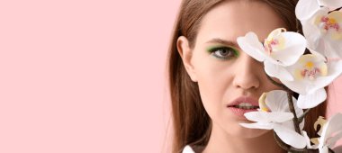 Güzel, genç bir kadın ve pembe arka planda orkide çiçekleri.