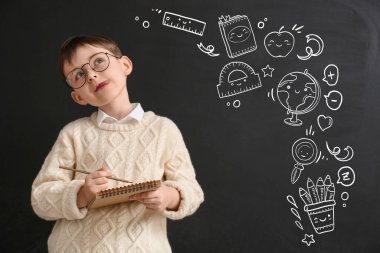 Karanlık arka planda not defteri olan düşünceli küçük okul çocuğu.