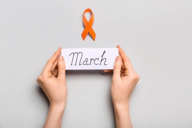 Elinde haber bülteni ve gri arka planda turuncu farkındalık kurdelesi olan bir kadın. Böbrek kanseri kavramı