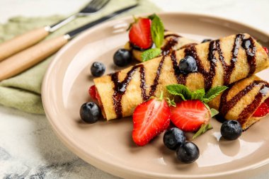 Beyaz arka planda böğürtlen ve çikolata soslu ince krep tabağı, yakın plan.