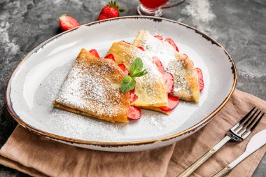 Üzerinde çilek, şeker tozu ve nane yaprakları olan ince krep tabağı, yakın plan.