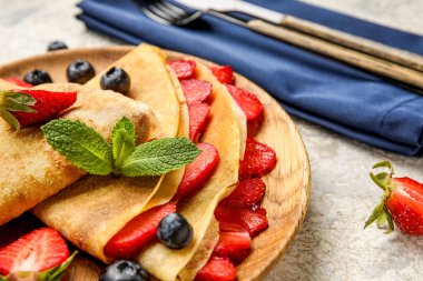 Arkaplanda nane yaprakları ve böğürtlenli ince krep tabağı, yakın plan.