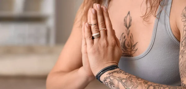 Beautiful tattooed young woman practicing yoga at home, closeup. Zen concept