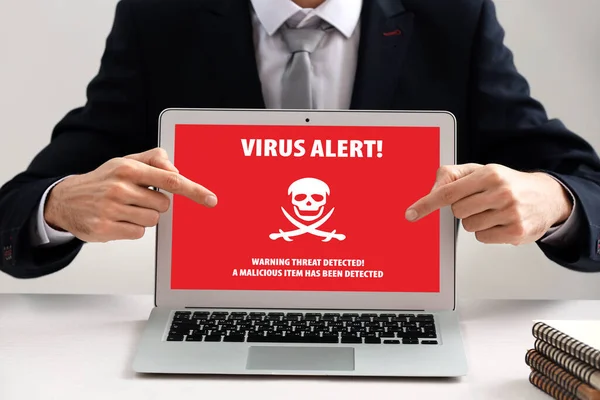 Young businessman pointing at laptop with text VIRUS ALERT. Antivirus concept
