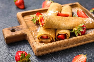 Koyu arkaplanda ince krep, çilek ve şeker tozu olan tahta, yakın plan.