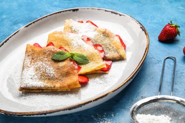 Mavi zemin üzerinde çilek ve şeker tozu olan ince krep tabağı