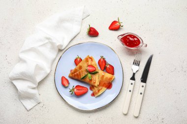 Beyaz arka planda çilekli, reçelli ve çatal bıçaklı ince krep tabağı.