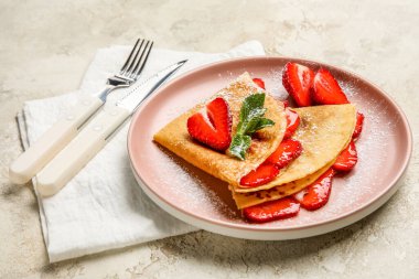 Üzerinde çilek, şeker tozu ve çatal bıçak bulunan ince krep tabağı.