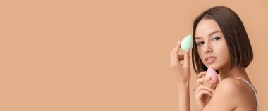 Bej arka planda makyaj süngeri olan genç ve güzel bir kadın.