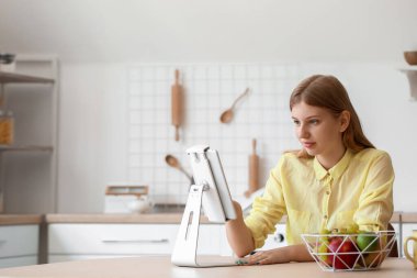 Genç kız mutfaktaki masada tablet bilgisayar kullanıyor.