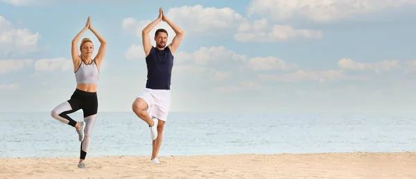 Sporty couple practicing yoga at sea resort. Zen concept