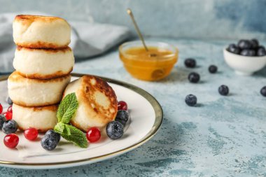 Bir tabak dolusu süzme peynir krep ve mavi arka planda böğürtlen.