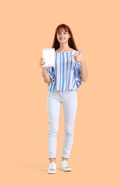 Teenage girl pointing at tablet computer on beige background