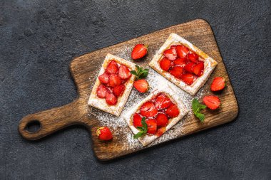 Koyu arkaplanda pudra şekerli ahşap tahta ve çilek.