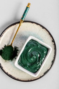Bir kase spirulina yüz maskesi ve arka planda barut, yakın plan.