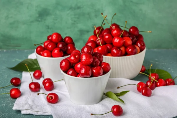 Bowls of sweet cherries on color background