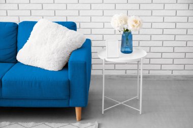 Oturma odasındaki mavi kanepenin yanındaki masada bir buket şakayık çiçeği olan vazo.