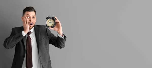 Stressed businessman holding alarm clock on grey background with space for text. Time management concept