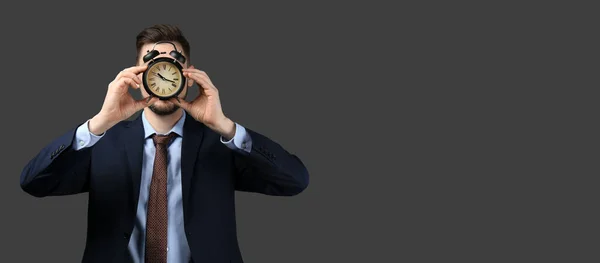 Businessman holding alarm clock on dark background with space for text. Time management concept