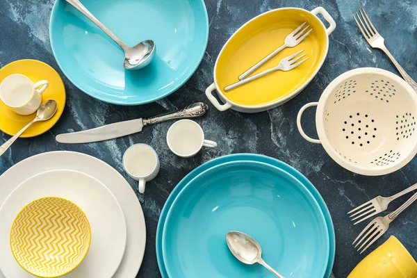 Colorful dinnerware and kitchen utensils on blue background