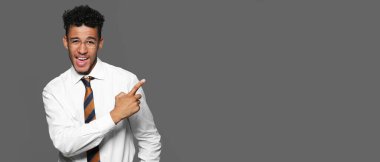 Yakışıklı Afro-Amerikalı iş adamı gri arka planda mesaj için yeri olan bir şeye işaret ediyor.