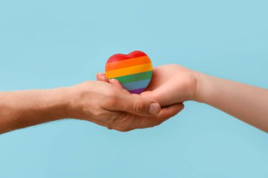 Mavi arka planda gökkuşağı kalpli erkek ve kadın elleri. LGBT kavramı
