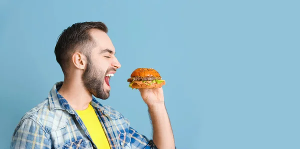 Junger Mann Isst Leckeren Burger Auf Hellblauem Hintergrund Mit Platz — Stockfoto