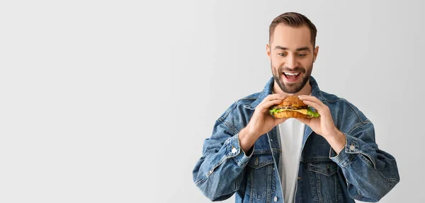 若い男食べるおいしいハンバーガーに光の背景でスペースのためのテキスト — ストック写真