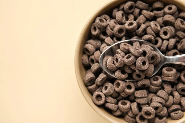 Bowl with black cereal rings on color background, closeup