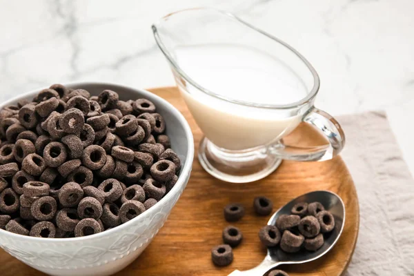 Bowl with black cereal rings and gravy boat of milk on light background, closeup