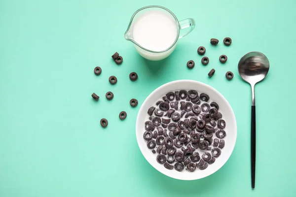 Composition with bowl of tasty cereal rings, milk and spoon on color background