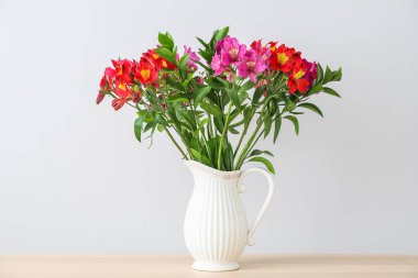 Astromerya çiçekli vazo. Ahşap masa üstünde, aydınlık duvarda.