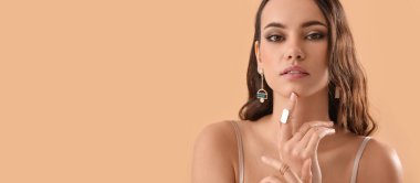 Bej arka planda şık mücevherler takan güzel bir genç kadın.