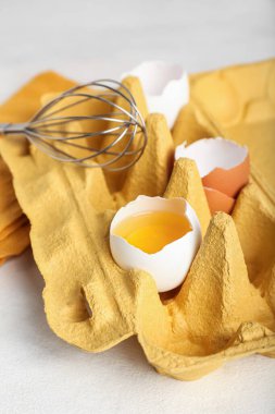 Kırık yumurtalı tutucu, kabuklu ve arka planda çırpmalı, yakın plan.