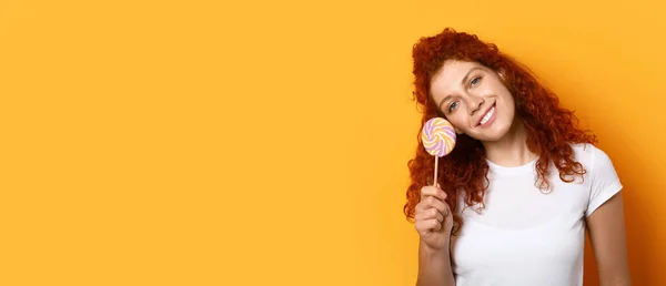 Beautiful redhead woman with lollipop on orange background with space for text