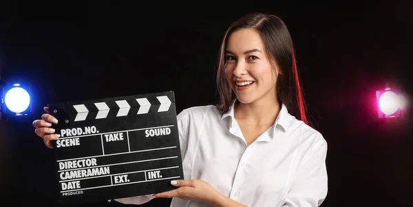 Young female film director with movie clapper on dark background