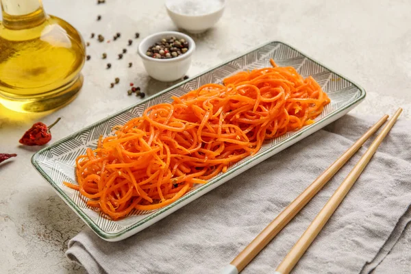 Bowl of spicy korean carrot and chopsticks on light background