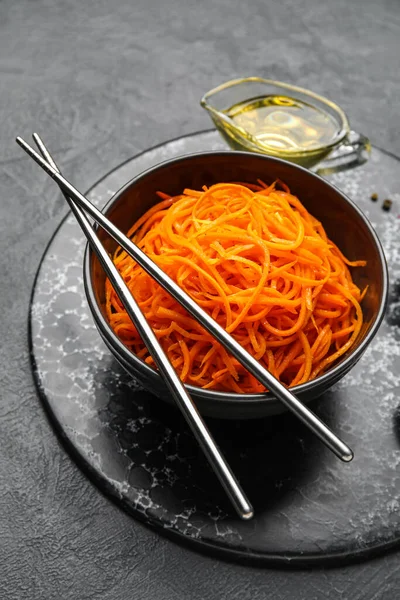 Board with bowl of korean carrot salad and chopsticks on dark background