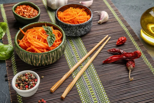 Bowls of tasty korean carrot salad, ingredients and chopsticks on table