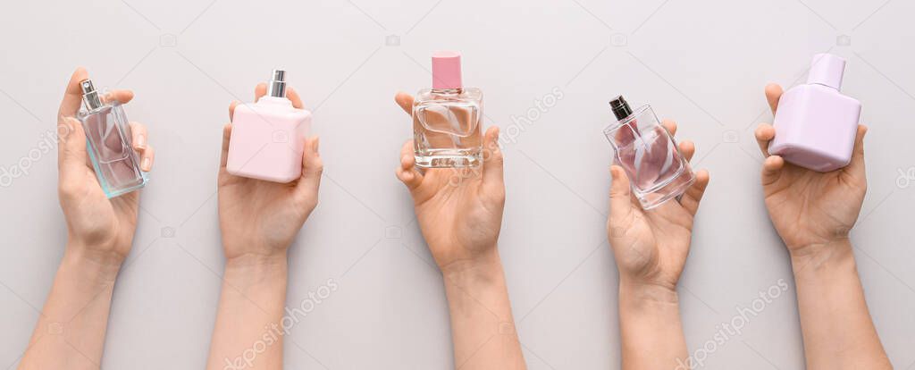 Female hands with bottles of perfumes on light background